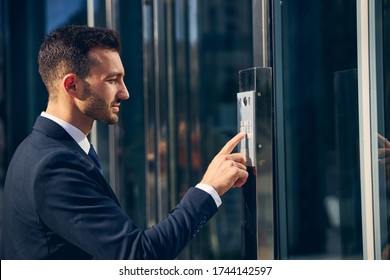 Handsome stylish businessman staying outside in formal clothes while pressing button on building with finger