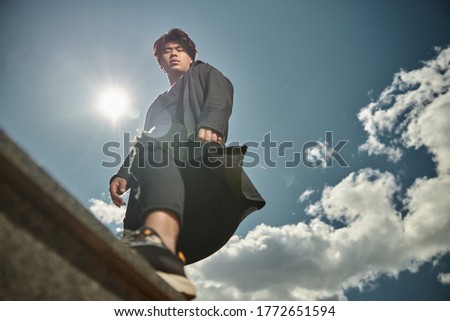 Handsome stylish guy looking at camera with serious expression while posing under blue cloudy sky