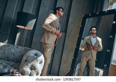 Handsome Stylish Man In Beige Suit At Home Looking At Mirror.