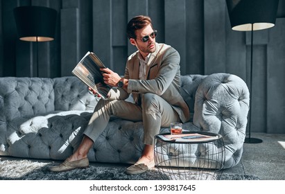 Handsome stylish man in beige suit at home sitting on sofa.