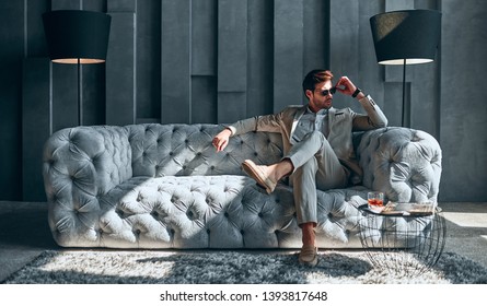 Schöner, stylischer Mann in beigem Anzug zu Hause sitzend auf dem Sofa.