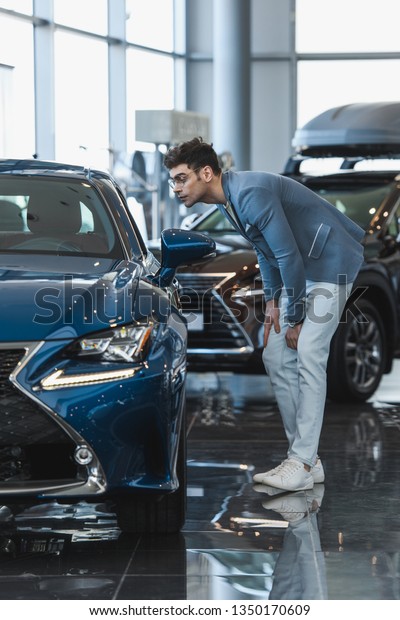 handsome stylish man in glasses standing near auto in\
car showroom 
