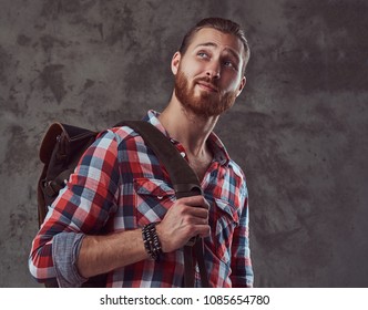 Handsome Stylish Redhead Traveler In A Flannel Shirt With A Backpack, Posing In A Studio On A Gray Background.