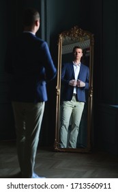 Handsome Stylish Tall Man In Blue Jacket And Beige Trousers At Home Looking At Mirror.