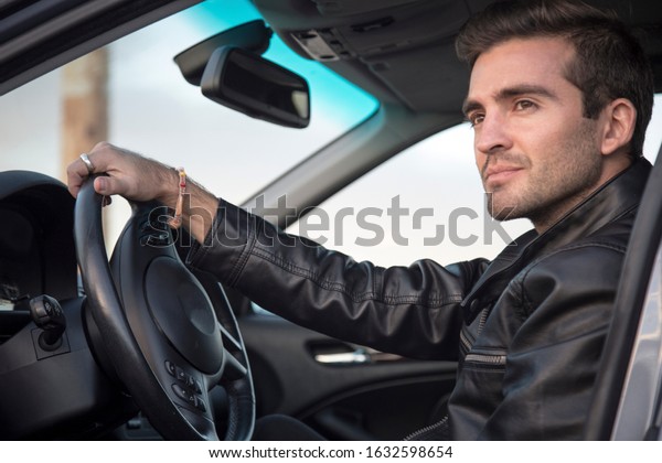 handsome and stylish white man in luxury car\
wearing sunglasses and leather jacket. A stylish male model with\
status looking out on beautiful\
sunset.