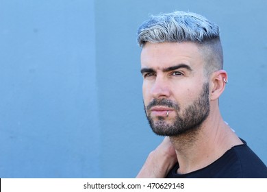 Handsome Stylish Young Man With Undercut Dyed Or Artificially Colored Hairstyle, Beard And Piercings Daydreaming Looking Away With Copy Space