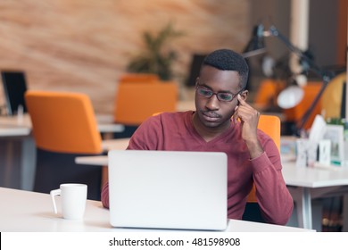 Handsome successful African American looking at the screen with serious face expression at modern startup office.