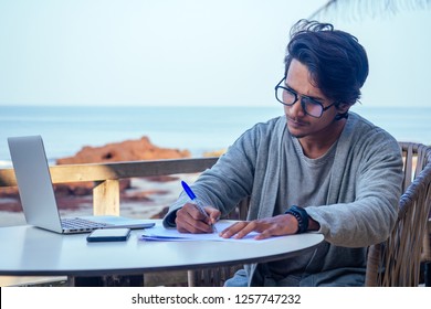 Handsome And Successful Indian Man In A Stylish Well-dressed Freelancer Working With A Laptop On The Beach.freelance And Remote Work.businessman Student In A Summer Cafe On The Shore Of India Ocean
