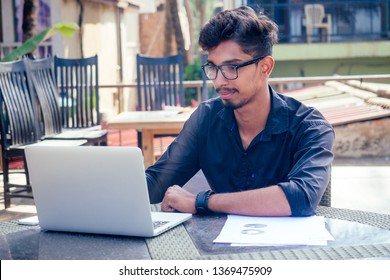 Handsome And Successful Indian Man In A Stylish Well-dressed Freelancer Working With A Laptop On The Beach.freelance And Remote Work.businessman Student In A Summer Cafe On The Shore Of India Ocean