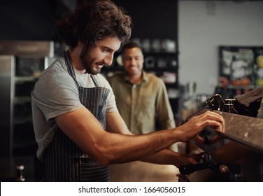 Handsome successful male worker making fresh coffee using machine while customer watching through counter - Powered by Shutterstock