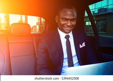 Handsome Successful Rich African American Business Men Entrepreneur In A Stylish Black Suit And Tie Sitting In A Luxury Car And Works With Laptop. Concept Of Luck And Currency Market Stock Exchange