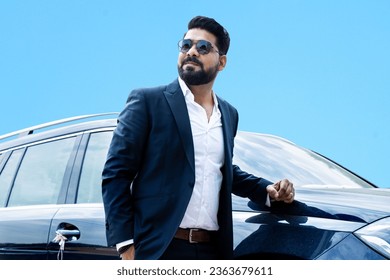 Handsome successful rich indian businessman in formal wear and sunglasses standing next to his car.
