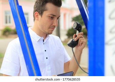 Handsome surprised man in a white shirt with a handset from a payphone in his hands.