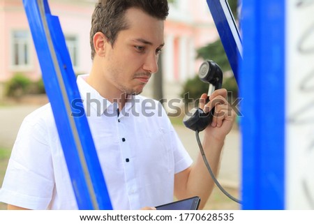 Handsome surprised man in a white shirt with a handset from a payphone in his hands.