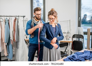 Handsome tailor measuring jacket on the woman client standing at the studio full of tailoring tools and equipment - Powered by Shutterstock