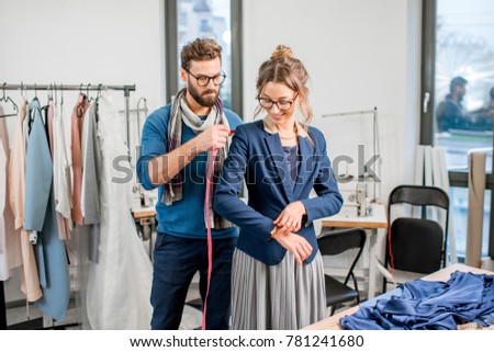 Handsome tailor measuring jacket on the woman client standing at the studio full of tailoring tools and equipment