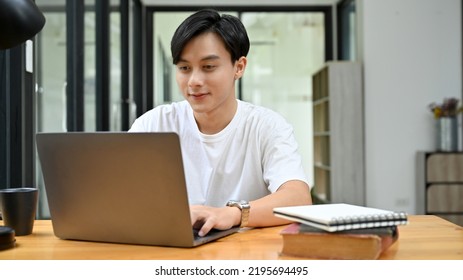 Handsome And Talented Young Asian Businessman In Casual Outfit Or College Student Working On His Project Assignment, Using Laptop Computer To Search An Online Informations.