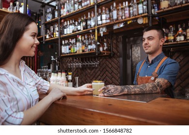 Handsome tattooed bartender serving a cocktail for his female customer