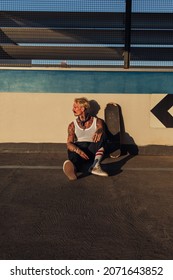 Handsome Tattooed Man Sitting On His Skateboard Outside During The Day