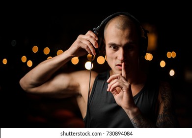 Handsome tattooed nightclub DJ in headphones feels the music on the background of night club lights - Shutterstock ID 730894084