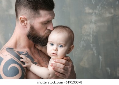 Handsome tattooed young man holding cute little baby on gray background