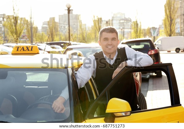 Handsome taxi driver standing near car with opened\
door on street