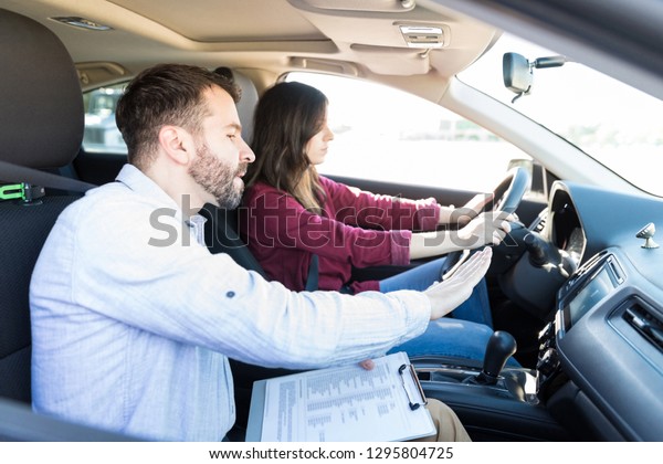 Handsome teacher gesturing while teaching car\
driving to female\
learner