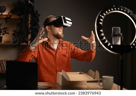 Handsome tech blogger male influencer unboxing device using modern smartphone while reviewing VR headset at home. Creating content for social media. Copy space
