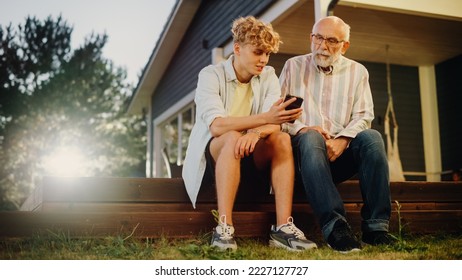 Handsome Teenage Grandson Teaching His Grandfather to Use a Smartphone. Young Man Showing Family Photos and Videos to His Grandparent. Relatives Sitting Outside on a Porch on a Nice Summer Day. - Powered by Shutterstock