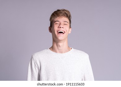 Handsome teenager guy 16-18 years old smiling and looking at the camera over gray background. Close up emotional portrait of caucasian young man
