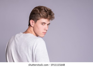 Handsome teenager guy 16-18 years old turning around and looking at camera over gray background.