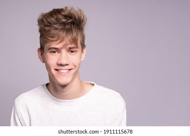 Handsome teenager guy 16-18 years old smiling and looking at the camera over gray background. Close up emotional portrait of caucasian young man