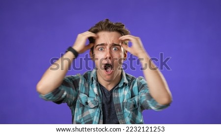 Handsome thinking young man 20s, looks at camera gives mind blown gesture showing explosion of ideas posing on purple background.