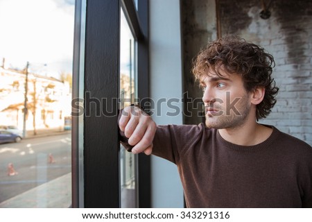 Handsome thoughtful guy in brown sweetshirt staring at the window
