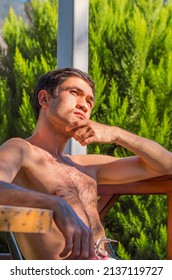 A Handsome Thoughtful Man Sitting Outdoors In A Green Garden In Morning Sunshine. Korean Male Person Sun Bathing Outside. Summer Leisure.