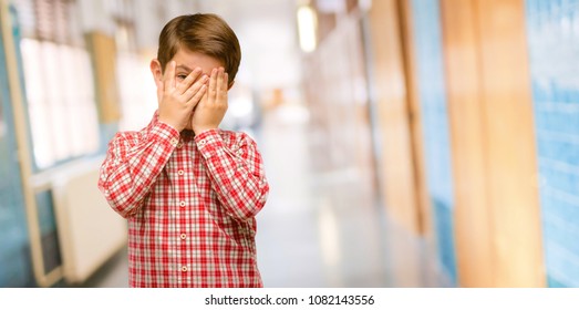 Handsome Toddler Child With Green Eyes Smiling Having Shy Look Peeking Through Fingers, Covering Face With Hands Looking Confusedly Broadly At School Corridor