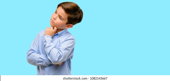 Handsome toddler child with green eyes thinking and looking up expressing doubt and wonder over blue background