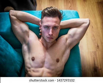 Handsome Totally Naked Muscular Young Man Laying Down On Couch At Home In Seductive Attitude, Looking At Camera