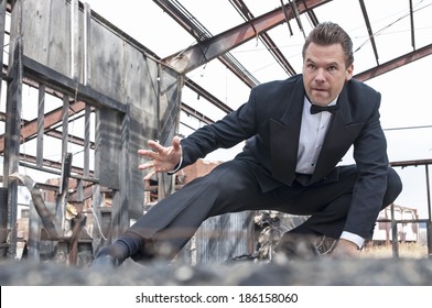 Handsome Tough Caucasian Man In Black Tuxedo Poses In Action Stunt Scene In Destroyed Warehouse