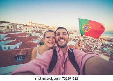 Handsome Tourists Couple Take Selfie Photo With View On Lisbon,Portugal From Miradouro On Sunny Clear Day Holding Portugal Flag.Honeymoon Loving Romantic Couple Traveling To European City For Holiday