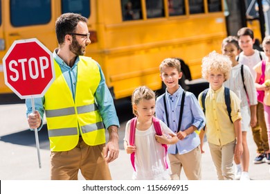 Handsome Traffic Guard Crossing Road With Pupils In Front Of School Bus