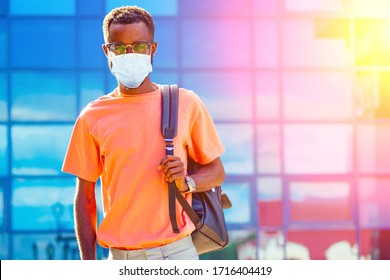 Handsome Trendy African Americans Nerd Male With Glasses In Stylish Clothes Colorful T-shirt With A Backpack On The Shoulders Stand Against The Background Of The Blue Windows Airport