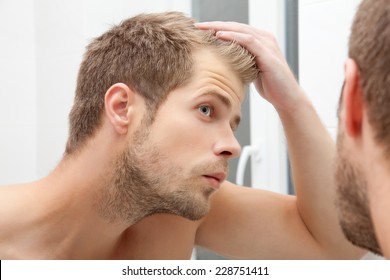 Handsome unshaven man looking into the mirror in bathroom - Powered by Shutterstock