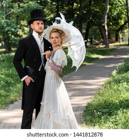 handsome victorian man standing with hand in pocket near woman holding umbrella 