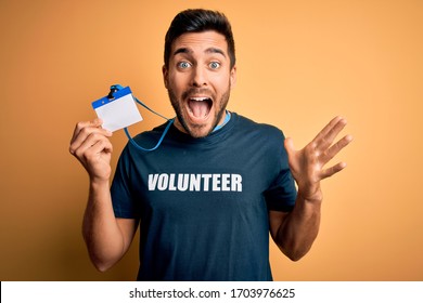 Handsome Volunteer Man With Beard Holding Id Card Identification Over Yellow Background Very Happy And Excited, Winner Expression Celebrating Victory Screaming With Big Smile And Raised Hands