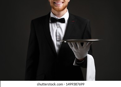 Handsome waiter with empty tray on dark background