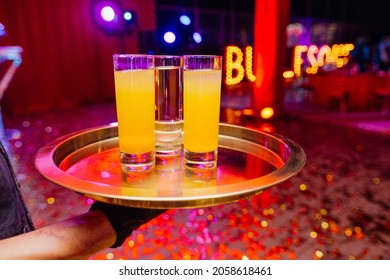 Handsome Waiter Holding In Naked Hands Tray With Glasses Full Of Cocktail. Night Party Celebration In Club With Colour Disco Lights. Professional Restaurant Serving In Banquet, Luxury Themed Event