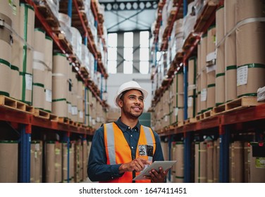 Handsome warehouse worker uses digital tablet for checking stock, on the shelves standing cardboard boxes - Powered by Shutterstock