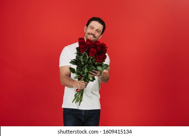 Handsome wearing white T-shirt, holding bouquet with red roses on red background. Celebrating Happy Valentine`s day