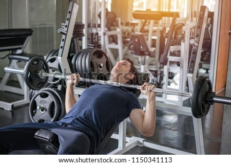 Handsome weightlifter lifting barbells bench press working out with curl bar in the gym.